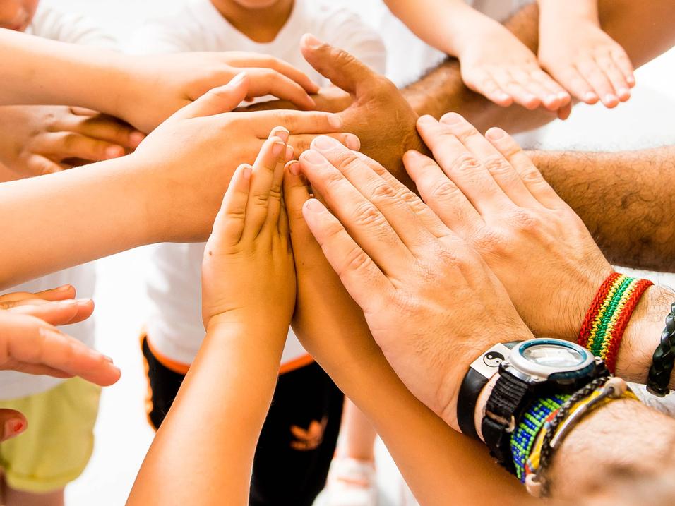 Kinder und Erwachsene legen ihre Hände in einem Kreis zusammen, symbolisieren Zusammenarbeit und Gemeinschaft.